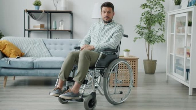 身体残疾男子的肖像坐在公寓的轮椅上看着相机