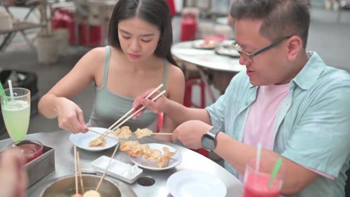 亚洲中国男性残疾人坐在轮椅上，女性朋友在八打灵街享受街头美食