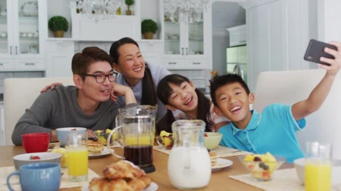 快乐的亚洲父母在厨房与儿子和女儿一起吃早餐，儿子集体自拍