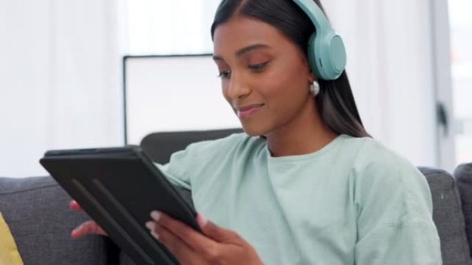 女人在社交媒体或互联网上听音乐时戴着数字平板电脑和耳机。快乐的印度女孩社交网络与移动设备，同时在家里