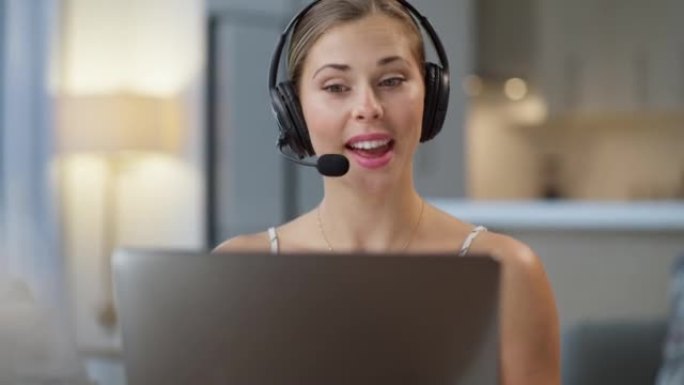 一个自信的年轻呼叫中心电话销售代理在办公室的笔记本电脑上进行虚拟视频通话时在耳机上交谈。友好的女性顾