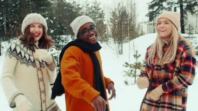 寒假。快乐有趣的多民族年轻朋友在白雪皑皑的森林慢动作中戴着温暖的帽子和衣服一起跳舞。