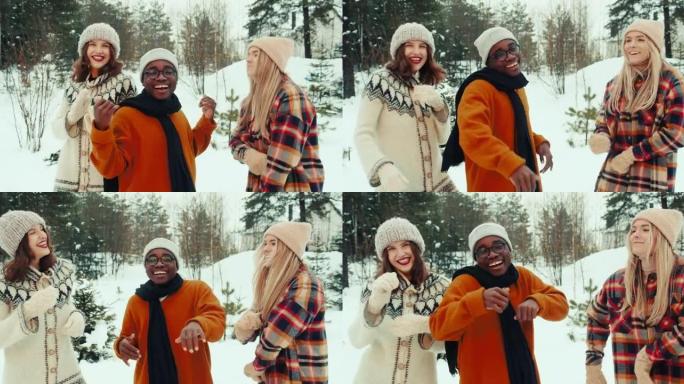 寒假。快乐有趣的多民族年轻朋友在白雪皑皑的森林慢动作中戴着温暖的帽子和衣服一起跳舞。