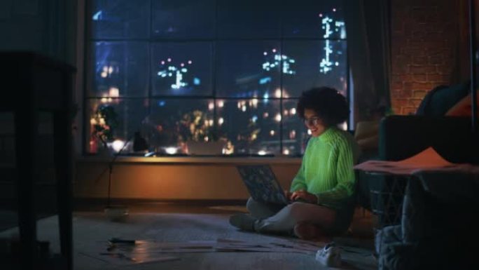 晚上，年轻的黑人妇女在时尚的阁楼公寓里使用笔记本电脑。富有创造力的女性微笑，查看社交媒体，浏览互联网