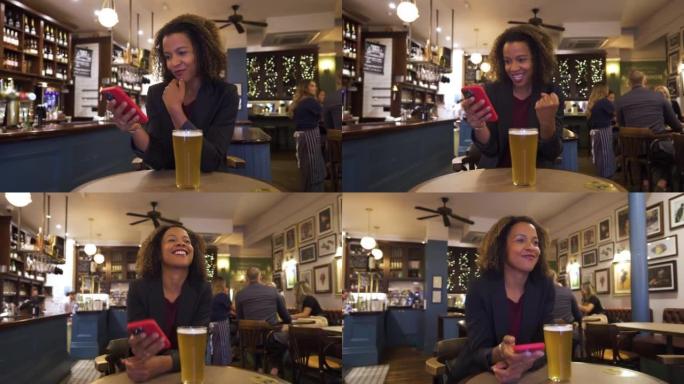 成功的女商人在酒吧喝啤酒的同时，在收到消息后检查智能手机并庆祝。