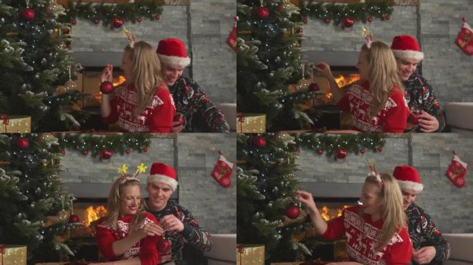 微笑的浪漫情侣在壁炉上用红色小玩意装饰圣诞树