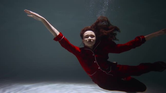 穿着红色睡衣的年轻美女的惊人电影肖像慢慢沉入水中入睡慢动作