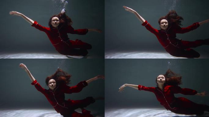 穿着红色睡衣的年轻美女的惊人电影肖像慢慢沉入水中入睡慢动作