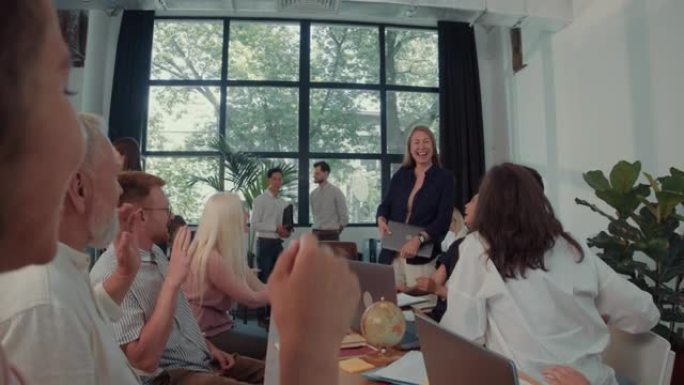 30岁快乐的年轻女商人进入办公室餐桌会议时，相机倾斜，带领各种同事慢动作。