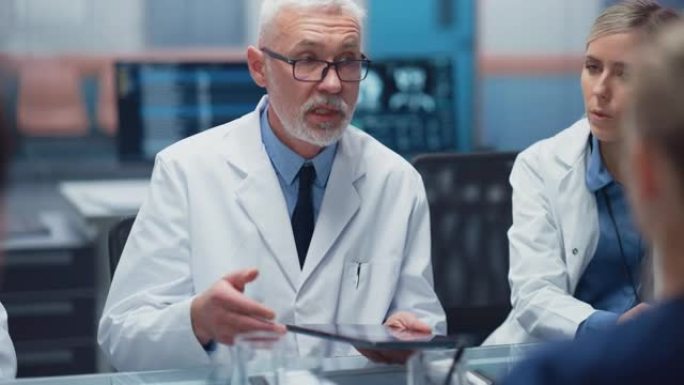 医院会议室: 高级男医师手持平板电脑，与医生团队讨论患者治疗。研究科学家谈论药物，药物开发