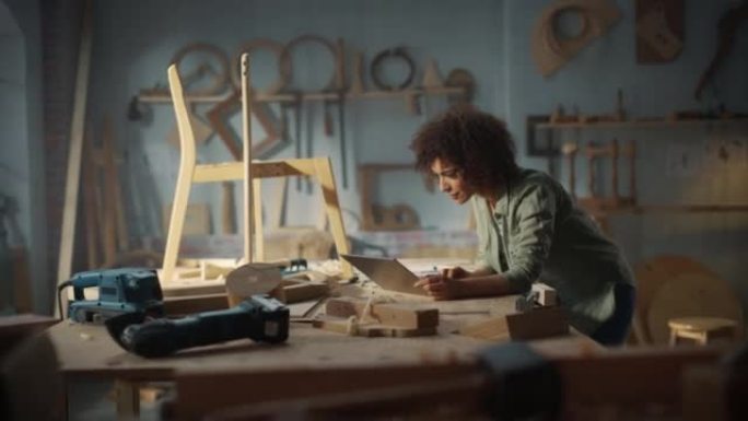 多民族女性木匠使用笔记本电脑在网上集思广益。黑人女性家具设计师在阁楼空间的工作室工作，墙壁上有工具。