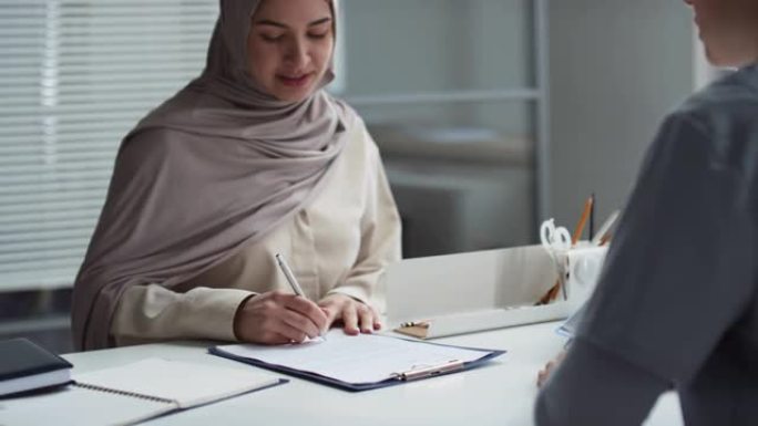 穆斯林女性患者在办公桌前签署文件并与医生握手