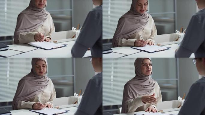 穆斯林女性患者在办公桌前签署文件并与医生握手