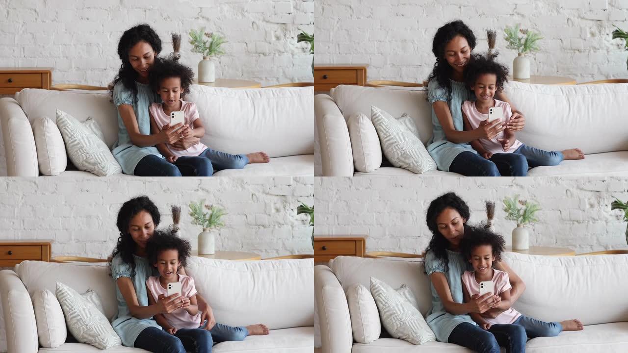 结合黑人妈妈女孩学龄前儿童在沙发上使用现代智能手机