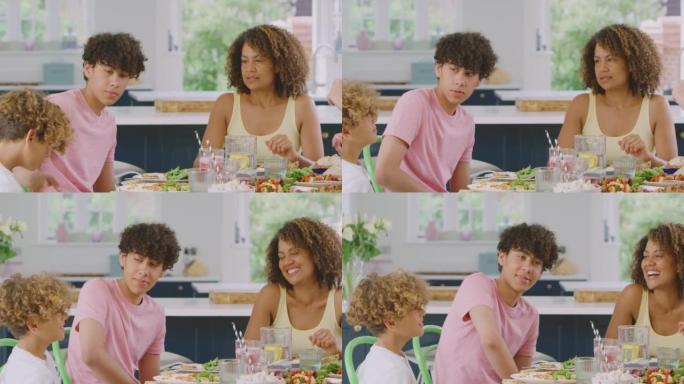多种族家庭的儿子坐在家里厨房的桌子旁一起吃健康的饭菜-慢动作拍摄