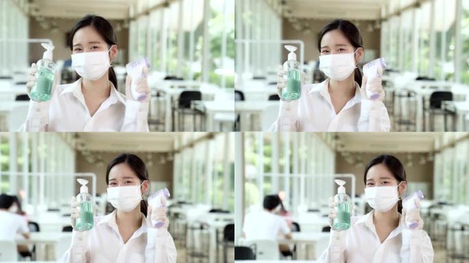 慢动作FHD淘: 亚洲女服务员戴着口罩和面罩，手持温度计和酒精凝胶洗手液，用于室内餐厅背景的清洁和卫