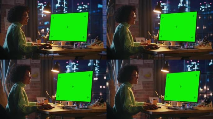 黑人女性创意员工在她的个人电脑上工作，在一个凉爽的阁楼空间里展示绿色大屏幕模型。积极的女孩对结果满意