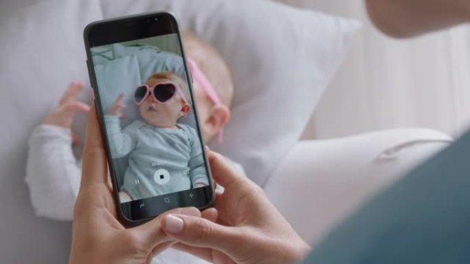 母亲用智能手机拍摄戴着太阳镜的有趣婴儿的照片，享受在社交媒体上分享母亲生活方式的可爱幼儿的照片