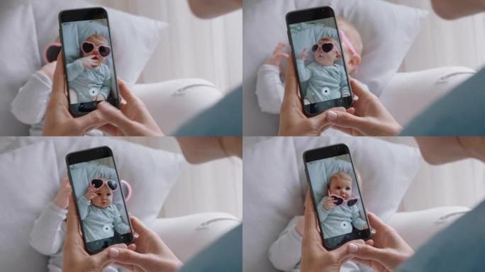 母亲用智能手机拍摄戴着太阳镜的有趣婴儿的照片，享受在社交媒体上分享母亲生活方式的可爱幼儿的照片