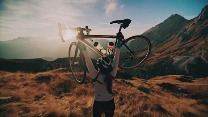 女骑车人在阳光明媚的风景秀丽的山区抬起自行车