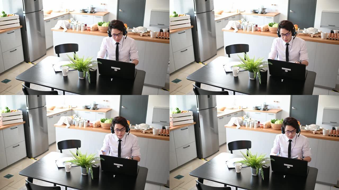 一名亚裔中国年轻人打着领带，穿着长袖衬衫和短裤，坐在餐厅里用笔记本电脑与他的商业伙伴和同事进行虚拟商