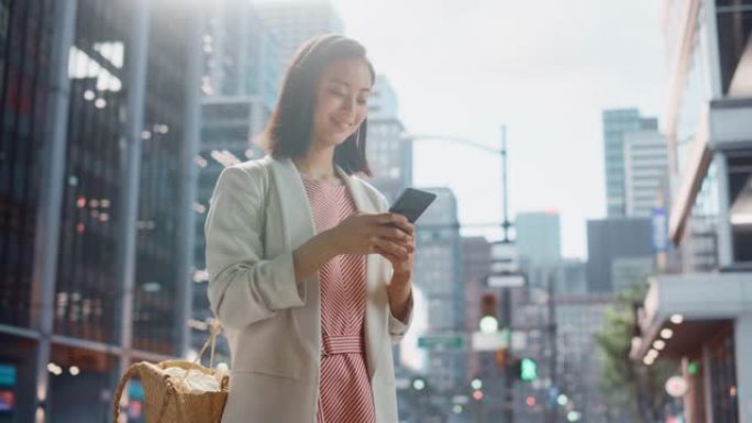 一位美丽的日本女性穿着时髦的休闲服，在城市街道上使用智能手机的肖像。大城市的经理与人们在线联系，消息