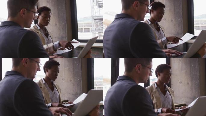 坐在咖啡馆里聊天的男女商业同事看着笔记本电脑和文书工作