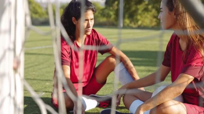 两名活跃的女足球运动员坐在足球场上聊天