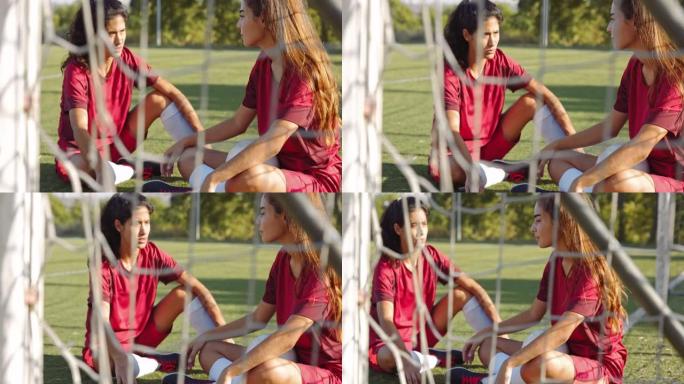 两名活跃的女足球运动员坐在足球场上聊天