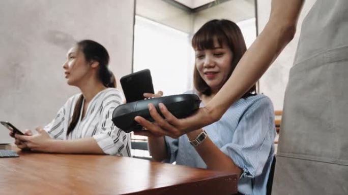 亚洲妇女在与朋友共进午餐后用智能手机在咖啡馆用餐