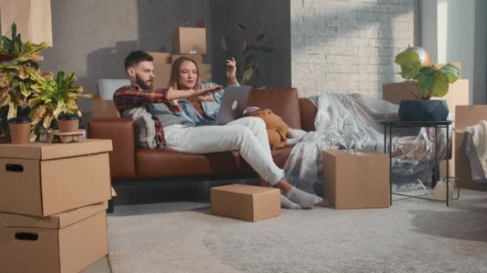 网上购买。年轻幸福的夫妇坐在新公寓的沙发上，在用笔记本电脑购物的搬运箱子里。