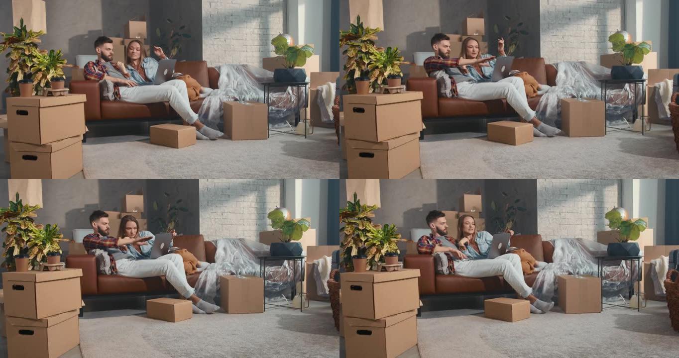 网上购买。年轻幸福的夫妇坐在新公寓的沙发上，在用笔记本电脑购物的搬运箱子里。