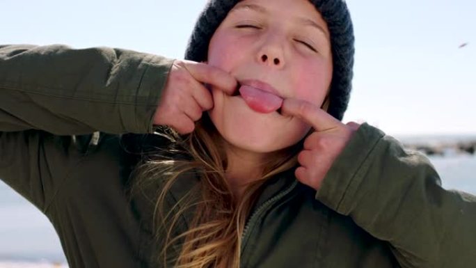 孩子，脸和快乐的女孩在海滩上穿着冬衣，吐舌头，对都柏林自然假期的有趣活动感到兴奋。表情有趣的肖像孩子