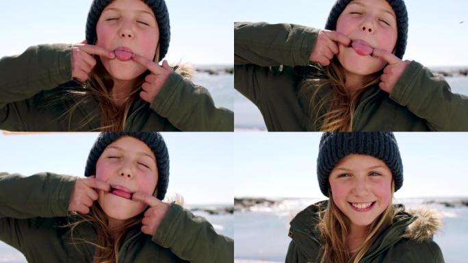 孩子，脸和快乐的女孩在海滩上穿着冬衣，吐舌头，对都柏林自然假期的有趣活动感到兴奋。表情有趣的肖像孩子