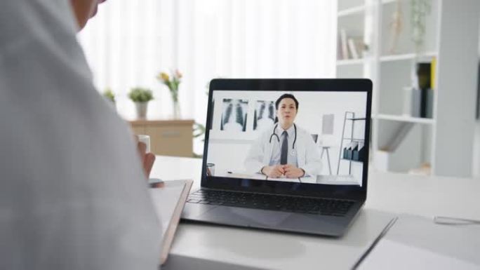 年轻的亚洲女士医生穿着白色医疗制服，使用笔记本电脑与健康诊所服务台的高级医生交谈视频电话会议。