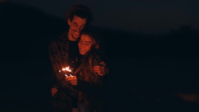 年轻夫妇在海滩上晚上抱着烟火