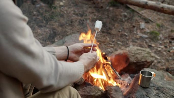 男性手的特写镜头将棉花糖放在棍子上，将甜点放在火上烤