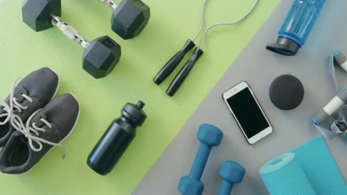 运动装备和设备的上方视图。平底鞋，智能手机，哑铃，水瓶，瑜伽垫，孤立在绿色，灰色背景。训练健身对象的