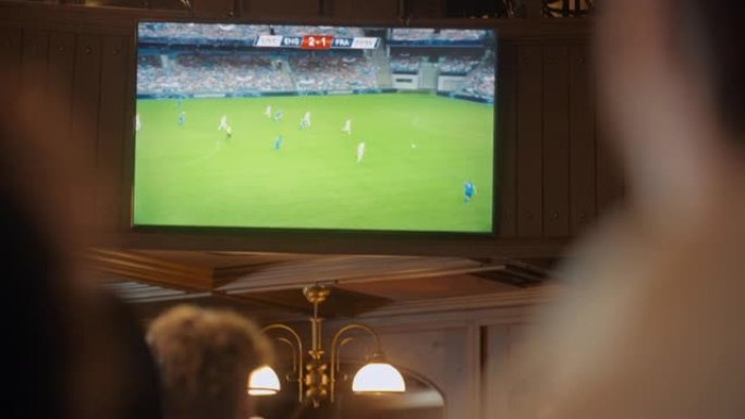 在体育酒吧观看现场足球比赛的足球迷的特写镜头。人们站在电视机前，为他们的团队欢呼。球员进球，人群庆祝
