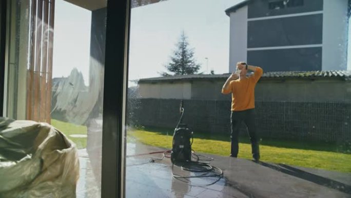 曼女士用智能手机拍照，同时用高压喷水清洁玻璃露台门