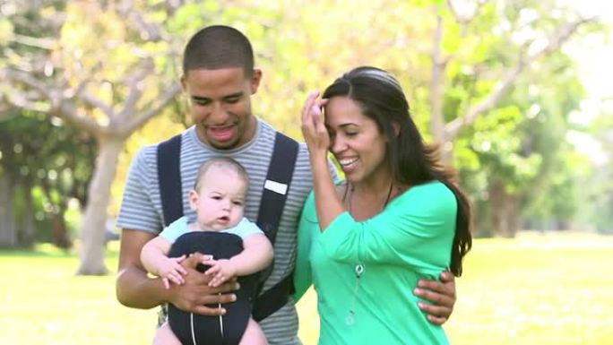 带婴儿背带在公园散步的家庭的慢动作镜头