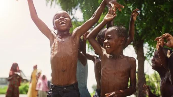 一群快乐天真的黑人儿童在长期干旱后玩耍并享受雨水的祝福。当水倒在他们身上时，真正的非洲孩子跳着笑。