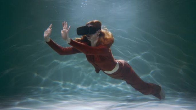 虚拟现实的概念。美丽的年轻快乐红头发的女人使用虚拟现实耳机漂浮在水下慢动作。