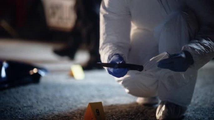 法医专家从犯罪现场挑选一把血淋淋的刀，并将其包装为证据。将凶器放在消毒容器中以保存指纹和痕迹的特写镜