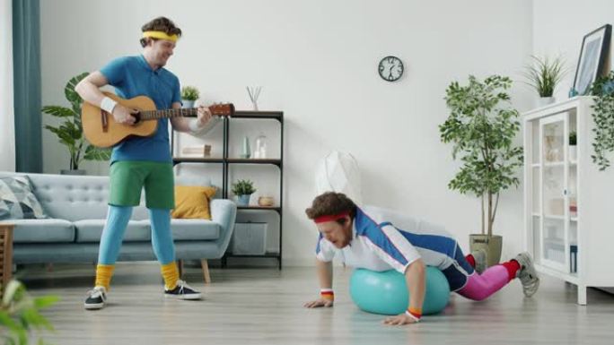 超重男子的慢动作与fitball一起锻炼，而朋友在家室内弹吉他
