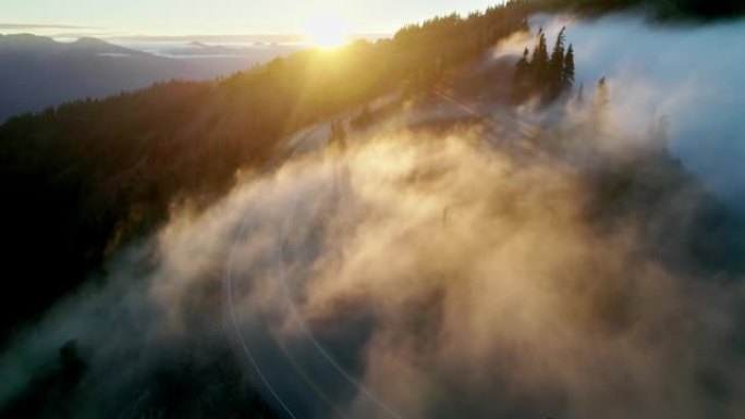 美国华盛顿奥林匹克国家公园的飓风岭。空中无人驾驶飞机在山上拍摄日落，阳光冲破雾气。日落时在云中飞翔。