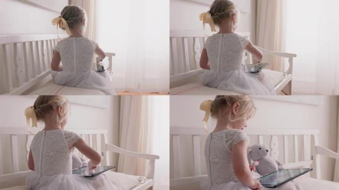 美丽的小女孩用平板电脑在触摸屏上画画享受创造力坐在长凳上，泰迪熊在家吃棒棒糖