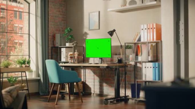 台式电脑显示器站在高度可调的桌子上，配有绿屏Chromakey模拟显示器。舒适的空阁楼公寓，桌子上有