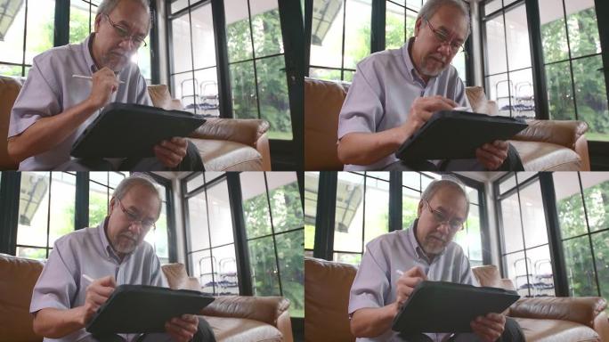 爷爷坐在工作中在家使用平板电脑，这是老年人用现代技术学习的东西。在没有病毒的检疫期间。