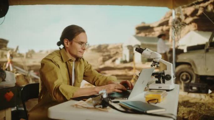 考古挖掘地点: 聪明的男性考古学家进行研究，使用笔记本电脑，分析化石遗骸，古代文明文化文物。历史学家